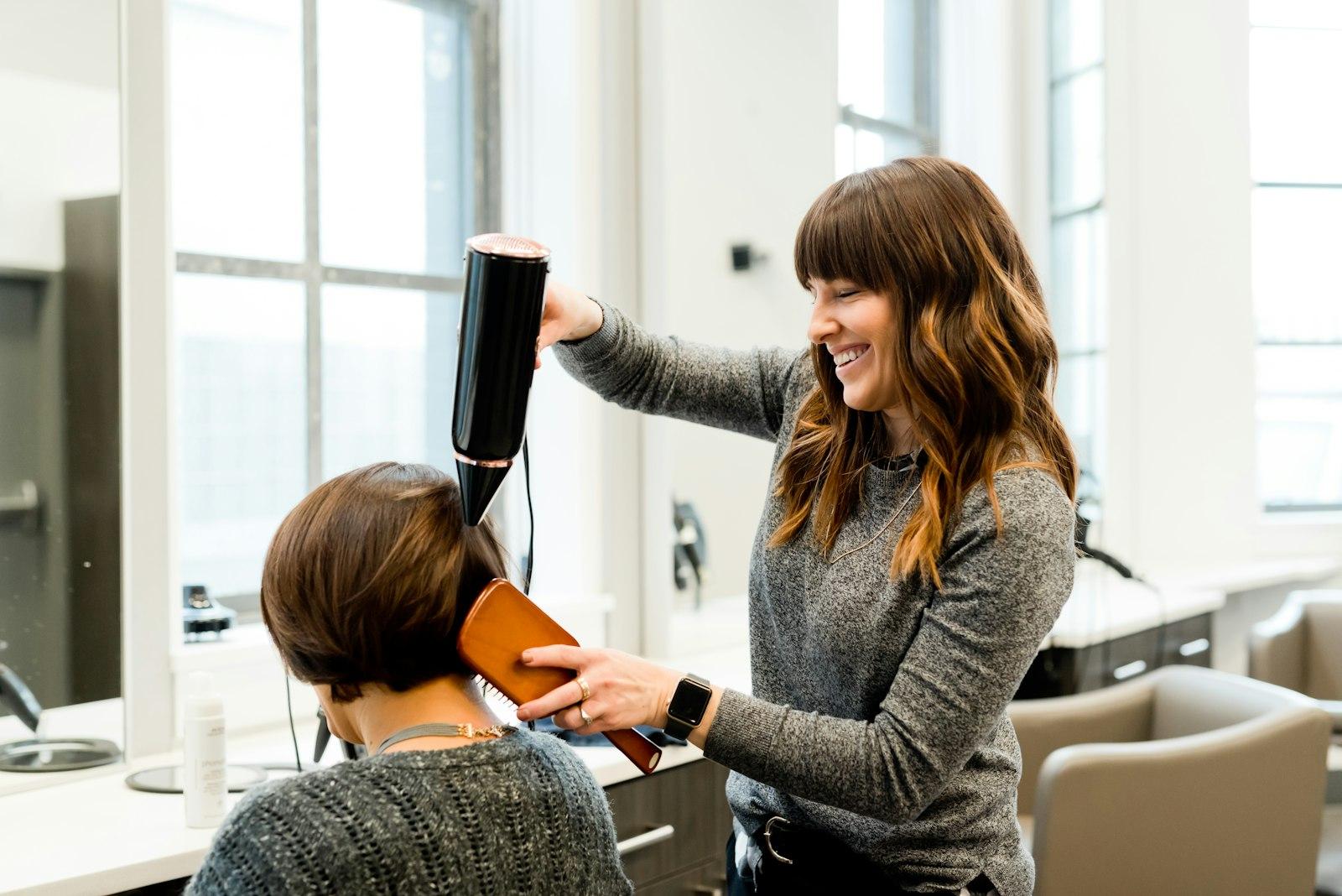 A stylist finishing a blow-dry at a bright salon station
