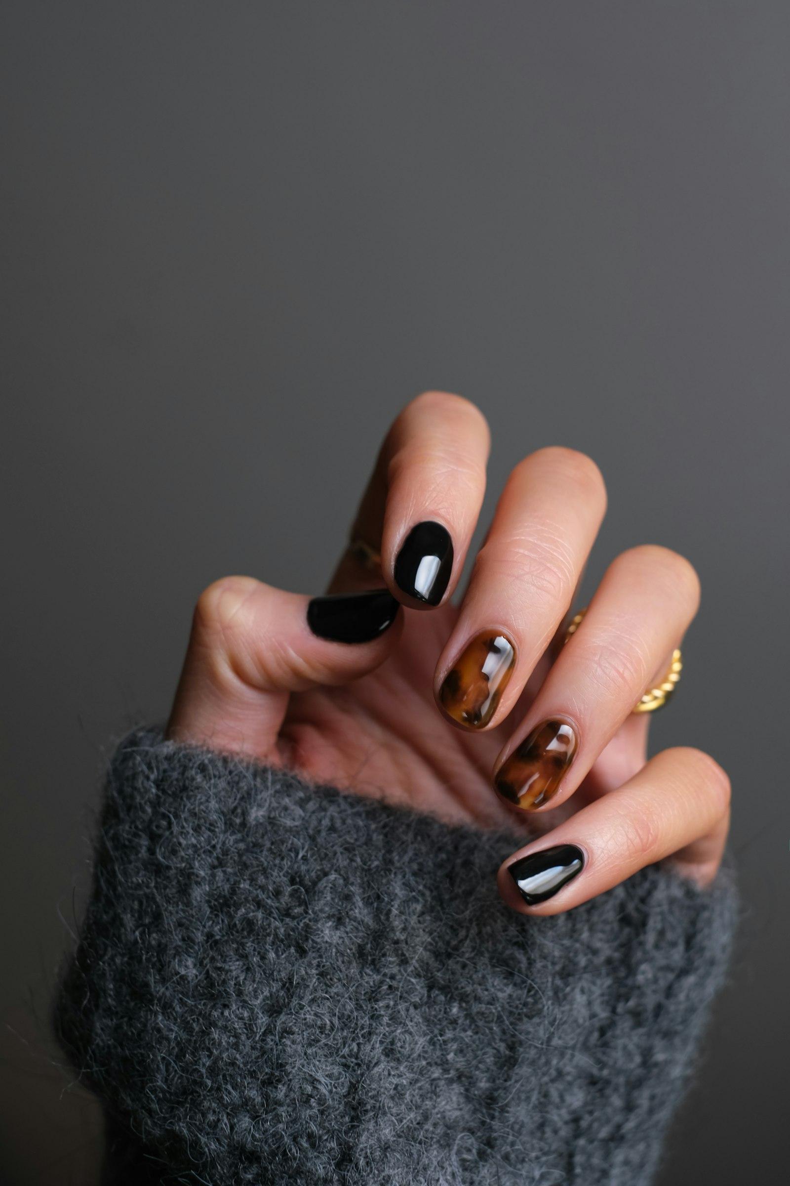 A hand with a precise black and tortoiseshell manicure